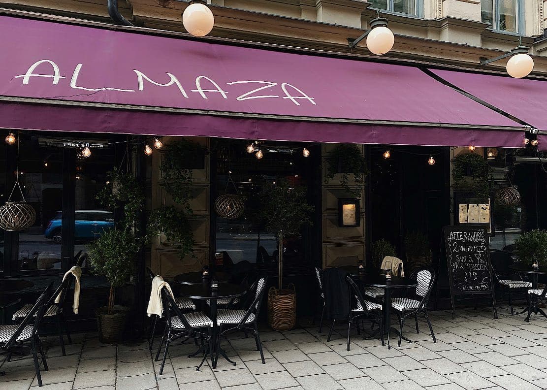 Almazas entré med lila markis och bord på trottoaren
